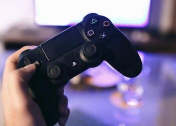 Free Person holding a gaming controller, blurred screen in background. Stock Photo